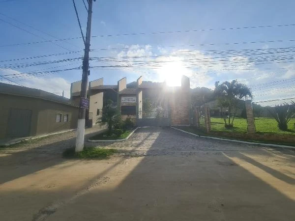 Apartamento em condomínio fechado com portaria e área verde ao redor sob céu azul com sol forte