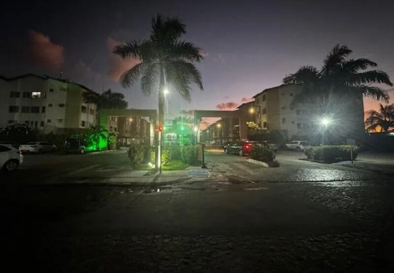 Apartamento no condomínio residencial Alpha Class à noite com iluminação pública e várias árvores no entorno