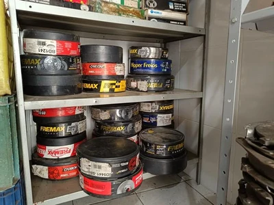 Vários tambores de peças automotivas armazenados em prateleira metálica dentro de galpão com paredes claras