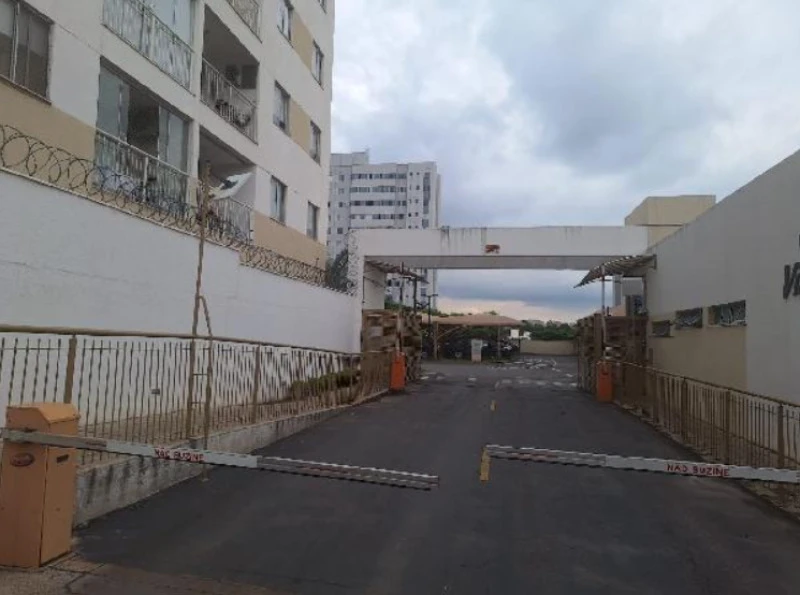 Apartamento branco em condomínio residencial com acesso por guarita e cancela de segurança em área urbana
