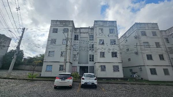 Apartamento branco em condomínio residencial com fachada simples e carros estacionados na rua de paralelepípedo
