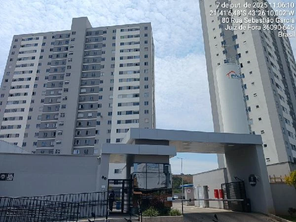 Apartamento em condomínio residencial com fachada branca e cinza e portaria com guarita de segurança