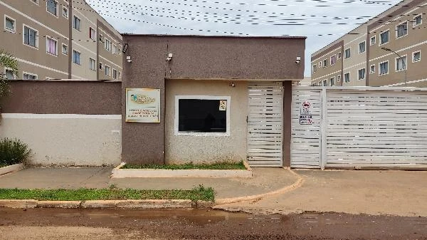 Apartamento em condomínio residencial com portaria e grades brancas, fachada cinza e prédios com várias janelas