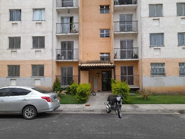 Apartamento com fachada em tons claro e pastel, varandas com grades, entrada principal com toldo e área verde frontal