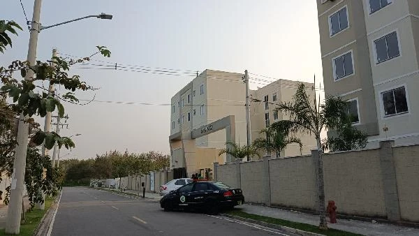 Apartamento bege em condomínio residencial com 2 blocos, portaria, calçada e carros estacionados na rua