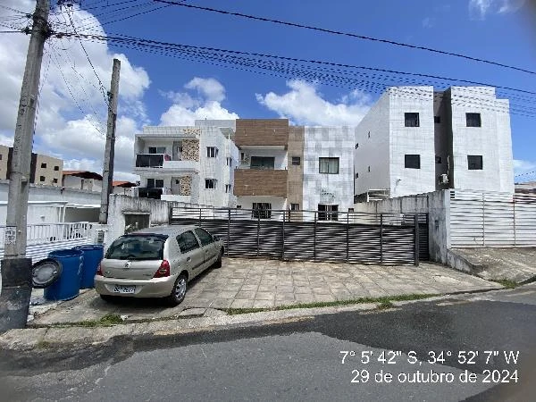 Apartamento branco com detalhes em pedra e madeira, condomínio com portão metálico em área urbana