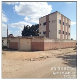 Apartamento bege de 63m² em prédio de três andares com muro alto e portão em área aberta de rua sem pavimentação