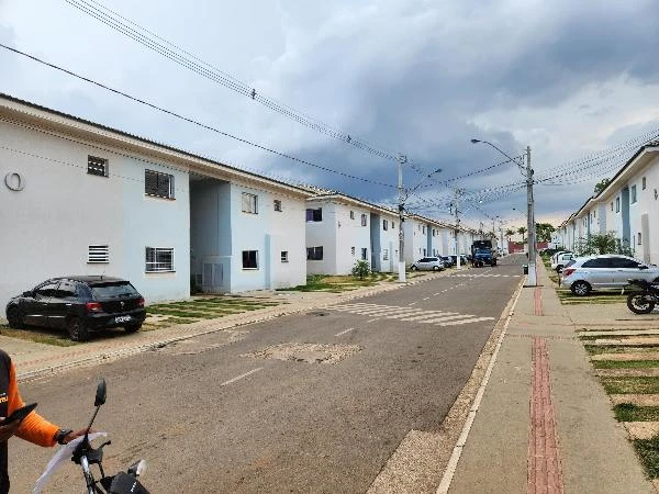 Apartamento branco com dois pavimentos em condomínio residencial com carros estacionados e céu nublado