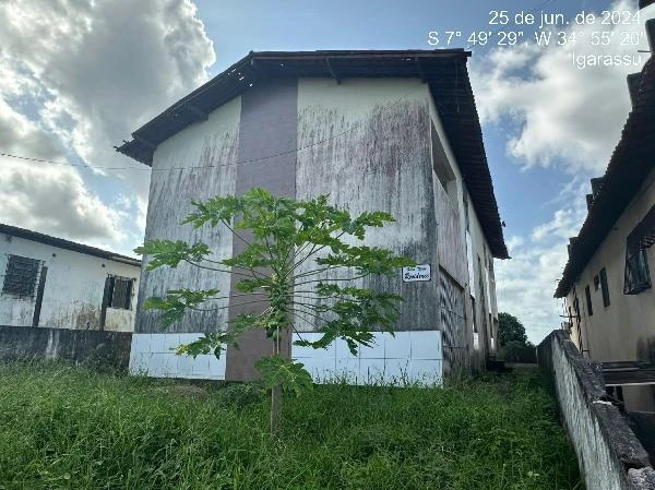 Apartamento branco com pintura desgastada e mato na frente em condomínio residencial