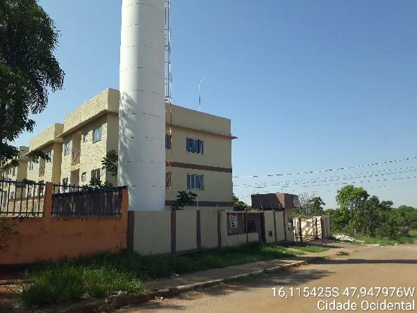 Apartamento bege de 2 andares com janelas azuis localizado em rua residencial com muro e cerca metálica