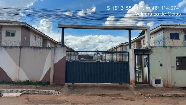 Apartamento em condomínio residencial com portão azul e muro branco em área urbana, sem avarias visíveis
