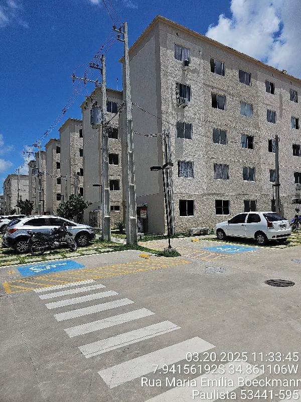 Apartamento bege em condomínio com quatro andares, estacionamento e área externa sob céu azul