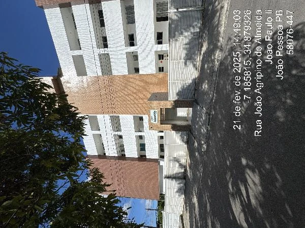 Apartamento em condomínio residencial com fachada de blocos claros e escuros, área externa com árvores e muro de proteção