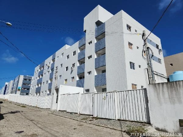 Apartamento branco em condomínio com várias unidades e muros brancos em rua residencial ensolarada