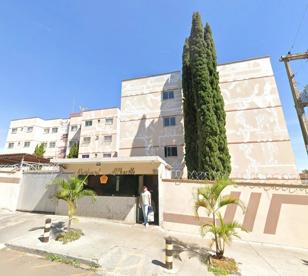 Apartamento em prédio residencial bege com cerca e guarita na entrada em área urbana com céu claro