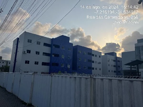Apartamento branco com detalhes azuis em condomínio residencial ao entardecer com grade branca em primeiro plano