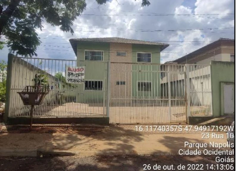 Apartamento de dois andares com pintura verde e rosa em área residencial cercada por portão branco e muro baixo