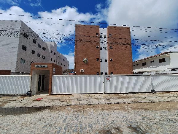 Apartamento com fachada em tons bege e branco, portão branco, localizado em área urbana com calçada e rua de paralelepípedos