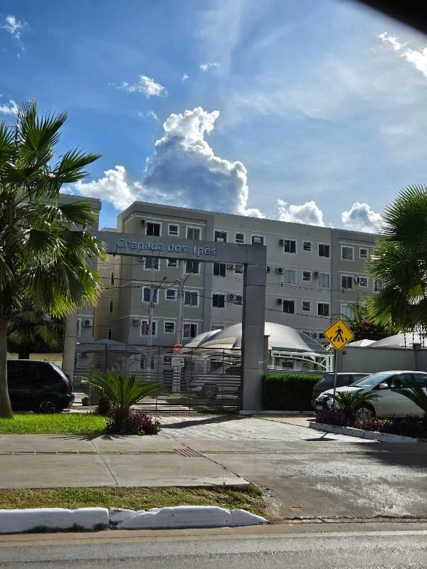 Apartamento branco no Condomínio Residencial Chapada dos Ipês com entrada principal e área de estacionamento dianteira
