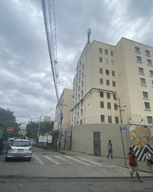 Apartamento em prédio claro com fachada em rua urbana e pessoas na calçada ao redor