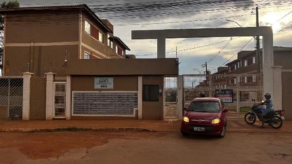 Apartamento marrom em condomínio com portaria e área de garagem, fachada em bom estado e via de terra