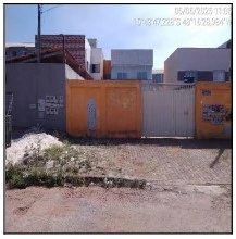 Apartamento com fachada simples cor laranja e branco em rua com chão de terra, sem avarias visíveis