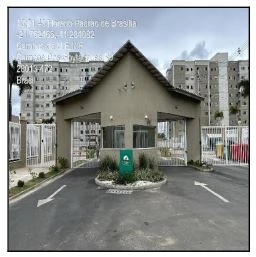 Apartamento no condomínio com fachada marrom clara e portaria central em área urbana com blocos residenciais ao fundo