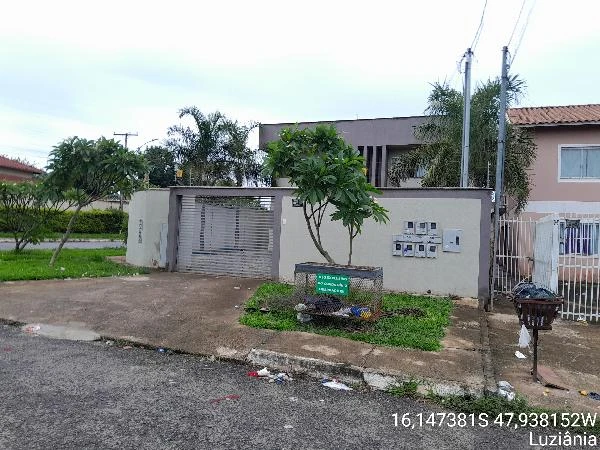 Apartamento com fachada de muro plano cinza, portão de metal, área verde e placas de correspondência em condomínio residencial