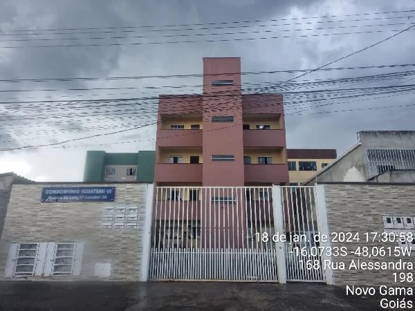 Apartamento rosa em condomínio residencial com fachada de quatro andares e portão branco em rua urbana sob céu nublado