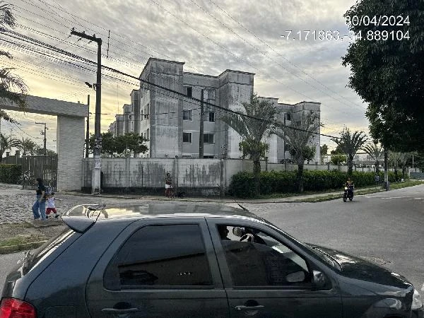 Apartamento cinza em condomínio com fachada de concreto e áreas verdes visíveis ao redor da rua
