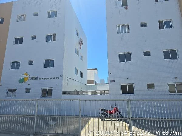 Apartamento branco de 41m² em condomínio residencial com cerca metálica e garagem descoberta com moto estacionada