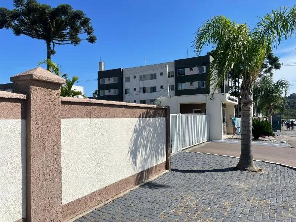 Apartamento em condomínio residencial com fachada moderna, muro baixo, portão branco e palmeiras na entrada