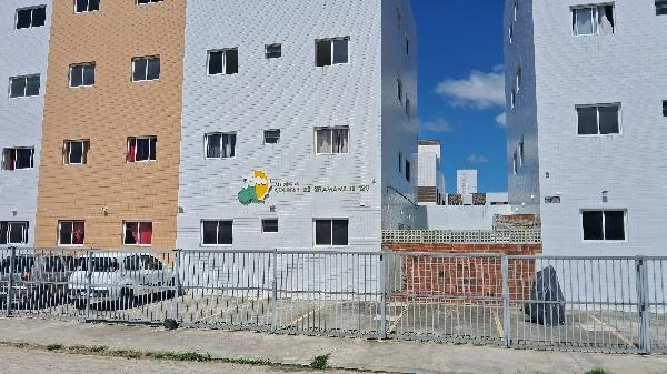 Apartamento branco e bege de 4 andares com grade na frente localizada em área urbana com céu claro