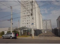 Apartamento branco com varanda em condomínio grande com muro e portaria, veículo branco estacionado em frente