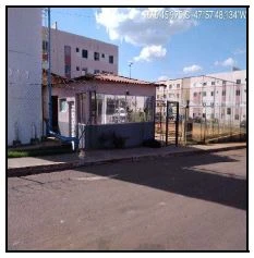 Apartamento branco em condomínio com portaria e prédios residenciais ao fundo sob céu azul