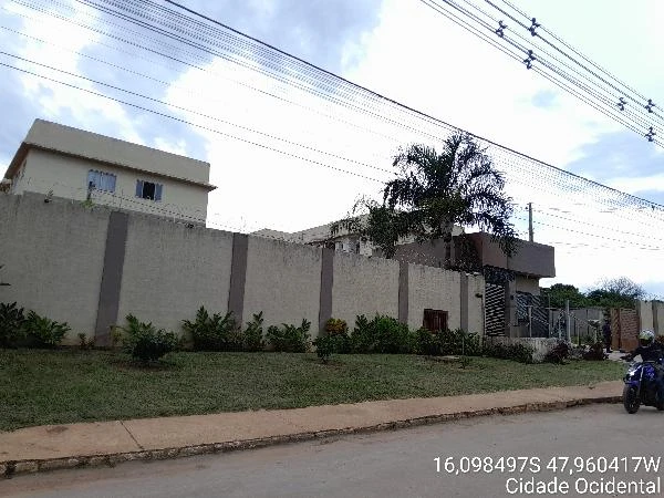 Apartamento em condomínio com fachada alta e muro cinza, área ajardinada na frente e motocicleta na rua