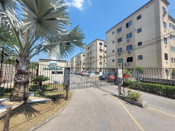 Entrada de condomínio residencial com portão e prédios ao fundo