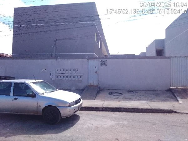 Apartamento branco em condomínio com muro alto e portão, localizado em rua asfaltada com carro estacionado na frente