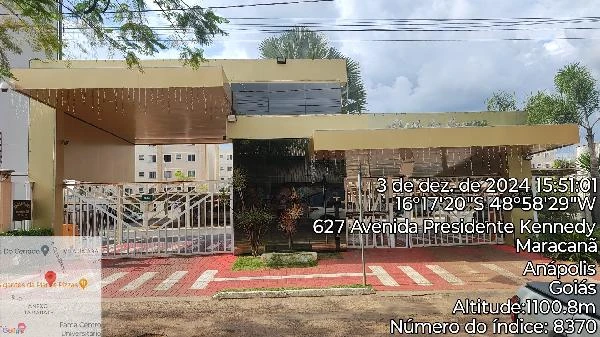 Apartamento com fachada em condomínio residencial com portão de metal branco e área verde na entrada