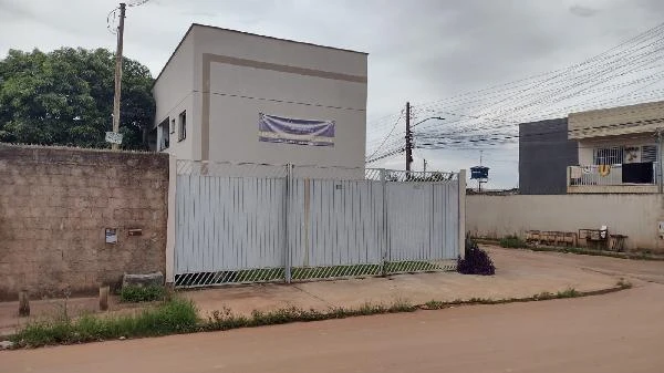 Apartamento cinza claro com portão branco em rua sem pavimentação e muro ao redor em condomínio