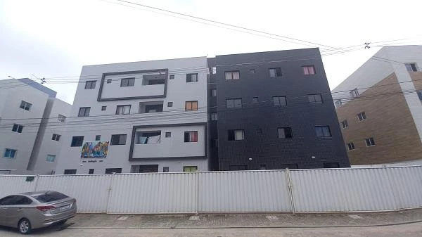 Apartamento branco e cinza com varanda e janelas visíveis em prédio de quatro andares com muro branco em área urbana