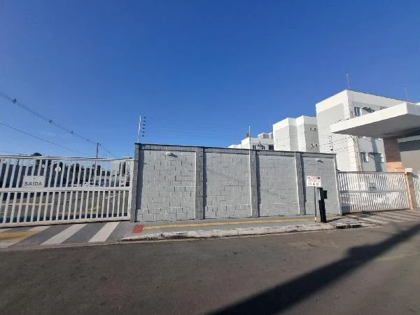 Apartamento branco em condomínio com muro e portão metálico em rua asfaltada sob céu claro