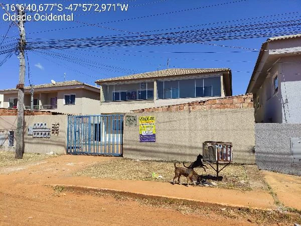 Apartamento em condomínio com fachada clara, portão azul e terreno com gramado em área urbana